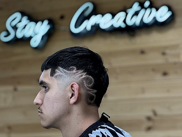 Perfil de un cliente con un diseño trazado sobre el fade, bajo el neón Stay Creative.