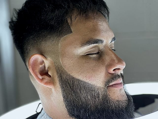 Perfil de un cliente con textura arriba, fade en los lados y la barba perfilada.